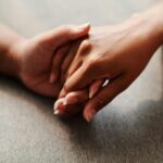 A close-up of two hands clasped together on a grey textile background, symbolizing unity.